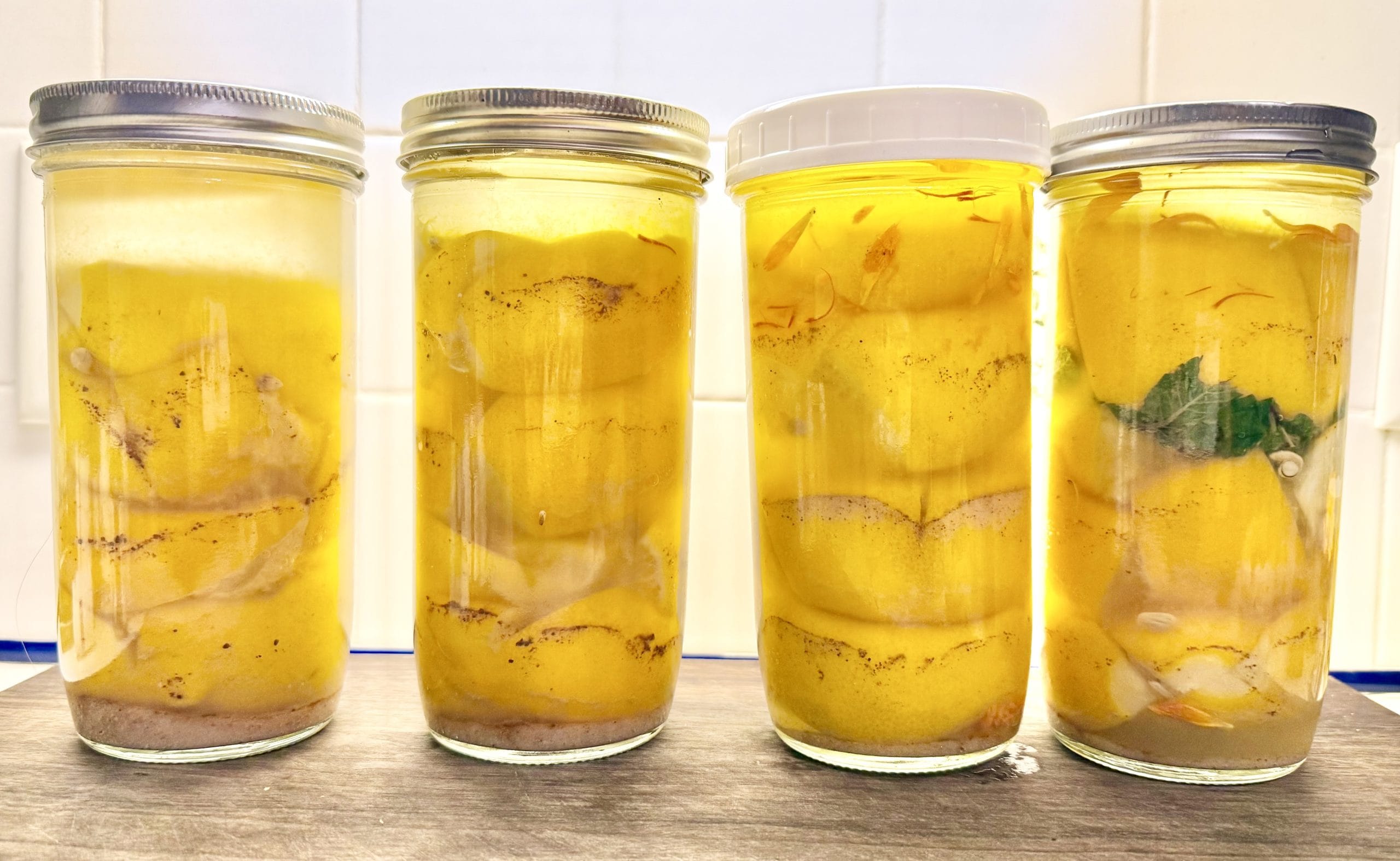 Four glass jars against a white wall, filled with preserved lemons and spices